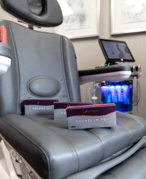 Juvéderm Volbella XC and Voluma XC injectable product boxes displayed on a gray aesthetic treatment chair in a medical spa treatment room.