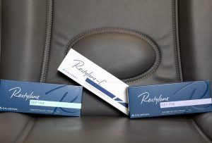 Restylane Defyne, Restylane-L, and Restylane Refyne dermal filler boxes arranged on a gray treatment chair.